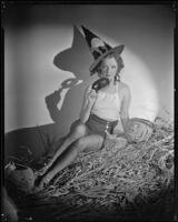 Inez Courtney, actress, wearing a witch's hat and sitting on a pile of corn, circa 1934-1939