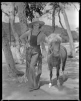 Inez Courtney, actress, wearing chaps and touching a pony, circa 1934-1939
