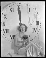 Inez Courtney, actress, holding a dog and sitting in front of a large clock, circa 1934-1939