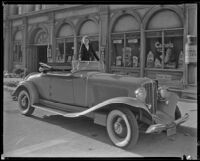 Babara Read, actress, standing in a car that is parked in front of a drug store, circa 1934-1936