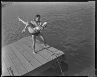 Johnny Mack Brown, actor, standing at the edge of a dock and holding a woman, Lake Arrowhead, circa 1929-1934