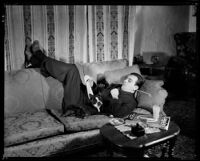 Fred Keating, actor, on a sofa with his dog in his Hollywood Hills house, Los Angeles, circa 1934
