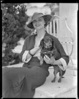 Woman wearing a hat and holding a dog in front of what may be the Hotel Del Monte, circa 1932-1939