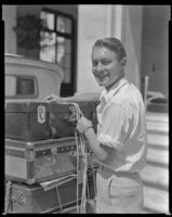 Man tying luggage onto a car, circa 1932-1939