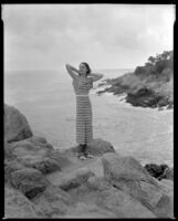 Woman standing on the rocks above the ocean, circa 1932-1939