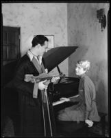 Joseph Schildkraut, actor, holding a violin while his wife, Marie, sits at a piano, circa 1934