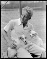 Gene Raymond, actor, sitting on a bench with two dogs, circa 1933