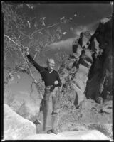 Gene Raymond, actor, wearing chaps and standing on a rock, circa 1933