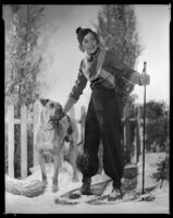 Woman wearing snowshoes and standing next to a dog, circa 1929-1934