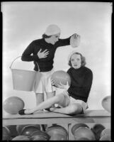 Inez Courtney, actress, sitting and holding a ball while Sheila Mannors, actress, holds a bucket and squeezes a sponge over her head, circa 1934-1938