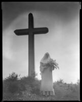 Billie Seward, actress, standing in front of a cross dressed as a nun, circa 1934-1935