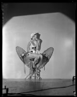 Billie Seward, actress, sitting on a stool holding a ball to her mouth with snowshoes behind her, circa 1934-1935