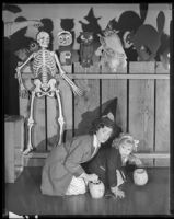 Edith Fellows and Dorothy Ann Seese, actresses, crouching in front of a fence covered with Halloween decorations, circa 1939