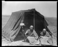 Two men sit in front of a tent, possibly in Tibet