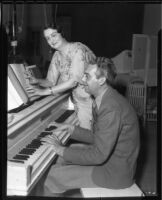 Arthur Johnston, composer, playing a piano as a woman identified as a blind pianist listens, circa 1936