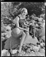 Marian Marsh, actress, sitting on a rock with a dog, circa 1935-1939