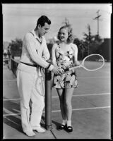 Marian Marsh, actress, standing on a tennis court with a man, circa 1935-1939