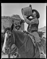 Colin Tapley and Earl Crawford seated on horseback, with Tapley drinking from a wooden bucket, on the set of Arizona, circa 1940