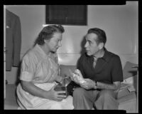 Humphrey Bogart holding a sandwich and sitting next to a woman, circa 1943-1956