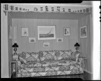 Couch with mugs and figurines on a shelf above it, on what may be a movie set, 1940s or 1950s