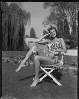 Rita Hayworth, actress, sitting in a chair wearing a bathing suit, circa 1940-1949