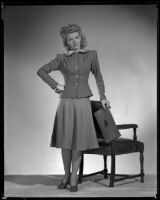 Woman standing next to a chair wearing a hat and holding a purse, 1940s