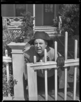 Smiley Burnette, actor, holding a gun and kneeling behind a fence, 1940s or 1950s