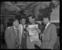 Tyrone Power, actor, joined by three men, reading an Indonesia brochure, circa 1955