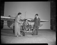 Man sitting in a glider as two men stand next to him (possibly during the filming of Gallant Journey), 1946