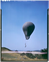 Man flying under a balloon while people watch from the ground (possibly during the filming of Gallant Journey), 1946