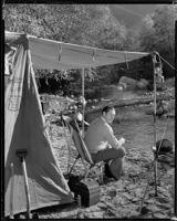 Jack Holt, actor, seated beneath a tent awning beside a stream, perhaps for a Movie Mirror magazine feature, 1927-1939