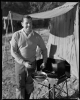Jack Holt, actor, cooking a fish on a camp stove beside a tent, perhaps for a Movie Mirror magazine feature, 1927-1939