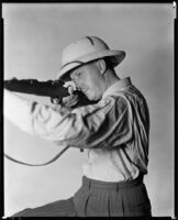 Clyde E. Elliott, producer and director, aiming a rifle, circa 1934