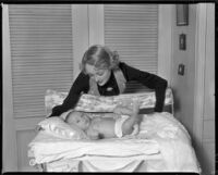 Sally Eilers, actress, leaning over her infant son, Harry Joe Brown, Jr., on his changing table, 1934