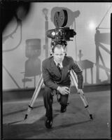 Albert Rogell, director, kneeling in front of a film camera, circa 1929-1938