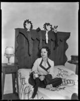 Geneva Mitchell, actress, sitting on a bed and putting a doll into a stocking, 1934