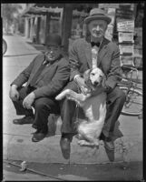 George Sidney, actor, sitting on a street corner next to Charlie Murray, actor, who is holding a dog, circa 1930-1934