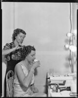 Leona Maricle, actress, drinking while a woman fixes her hair, circa 1936-1938