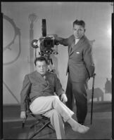 Laurence Stallings, screenwriter, standing next to a film camera while Lewis Milestone, director, sits next to him, circa 1933