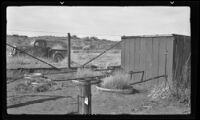 Planting tanks and irrigation pipes emerging from a shed in a fenced off area beside a road and truck, southern California, circa 1942