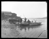 Men load rowboats on the beach.